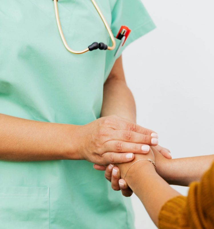 A nurse in green scrubs gently clasps a patient's hand, offering support.