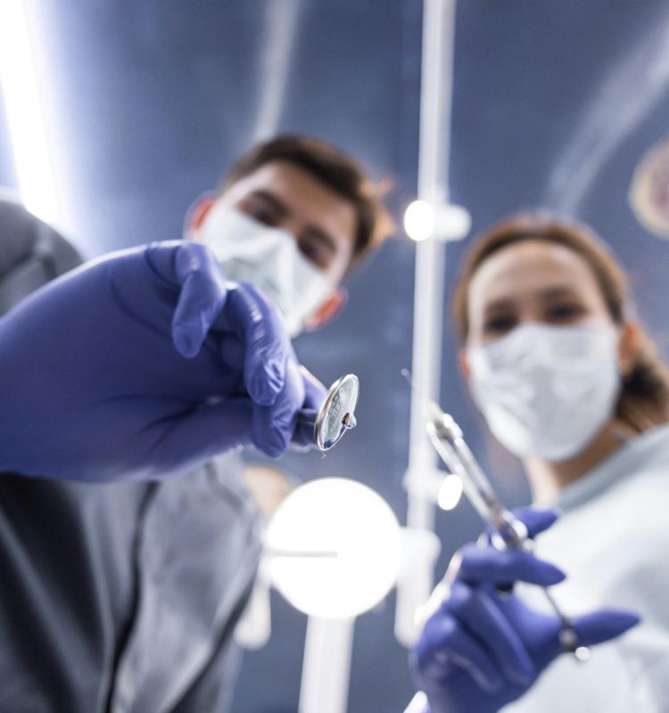 Two dentists in masks and gloves holding dental tools from a low angle view.